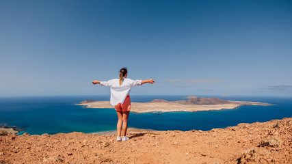 Viewpoint to La Graciosa from Lanzarote and happy traveller woman. View of La Graciosa Island and blue ocean