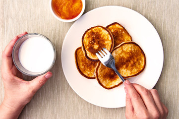 Breakfast.Two female hands, a fork, a plate with pancakes, a glass of milk and a saucer of jam, breakfast.