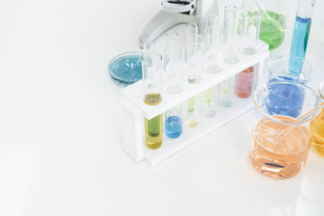 Set of test tubes and beakers with color solutions on a white desk in a laboratory setting.