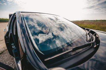 Cute baby girl sits inside the car and looks in the windshield on the beautiful sky. Closeup