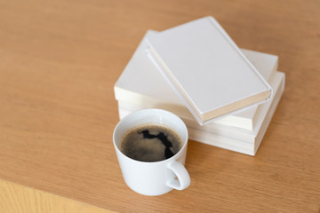 Cup of coffee with blank closed white book on wooden table for morning refreshment. Concept lifestyle comfortable working at home