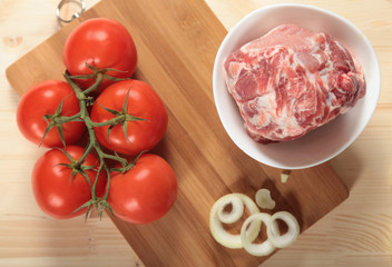 branch of tomatoes, meat and onion against the cutting board
