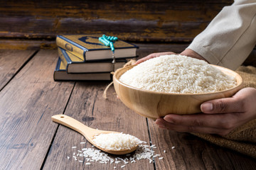 Hands holding a wooden bowl of rice grains for zakat, Islamic zakat concept. Muslims to help the...