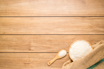 A pile of rice seeds in a wooden bowl that is placed in a sack and a wooden spoon placed on a wooden table, with copy space, top view.
