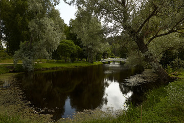 Beautifull pond in Puskin's motherland Mikhailovskoe. Green park with a small lake and white arch bridge. Water reflects trees and sky