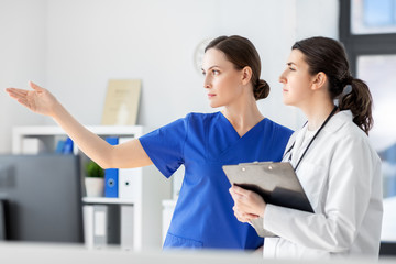 medicine, healthcare and people concept - nurse showing something to doctor with clipboard at hospital