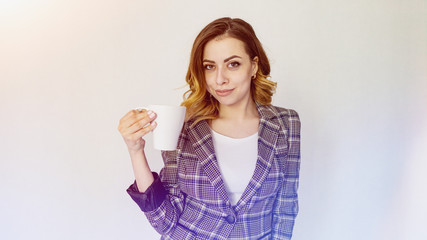 happy girl is standing with a cup of coffee and looking at the camera. beautiful girl in a checkered jacket is drinking coffee