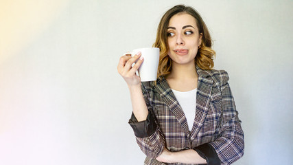 happy girl looks at a cup of coffee and licks her lip. beautiful girl in a checkered jacket is drinking coffee