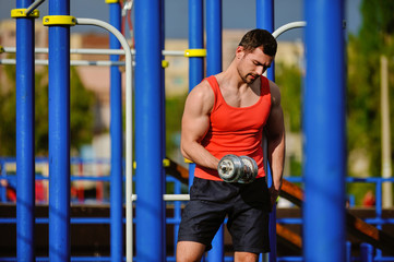 Obraz premium Young sports guy is doing exercises with dumbbells at the playground.