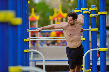 Young strong guy pulls himself up on the horizontal bar.