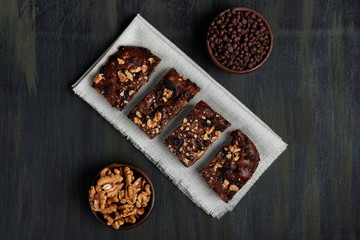 pieces of chocolate brownie and walnuts next to walnuts and chocolate in clay pots in the foreground