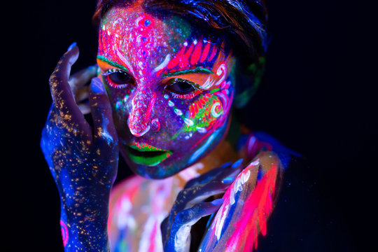 Fashion model woman in neon light, portrait of beautiful model girl with fluorescent make-up, Body Art design of female disco dancer posing in UV, painted face, colorful make up, over black background