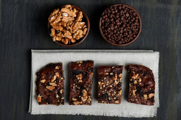 pieces of chocolate brownie and walnuts next to walnuts and chocolate in clay pots in the foreground