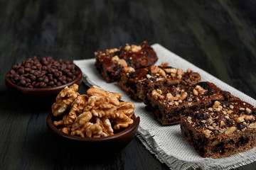 pieces of chocolate brownie and walnuts next to walnuts and chocolate in clay pots in the foreground