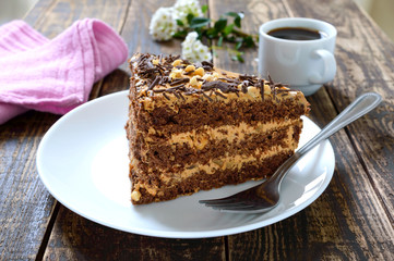 Chocolate cake with nut cream on a wooden table. A piece of cake on a plate and a cup of coffee.