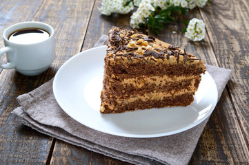 Chocolate cake with nut cream on a wooden table. A piece of cake on a plate and a cup of coffee.