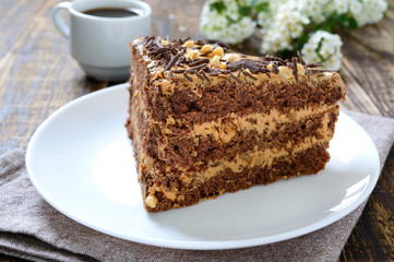 Chocolate cake with nut cream on a wooden table. A piece of cake on a plate and a cup of coffee.