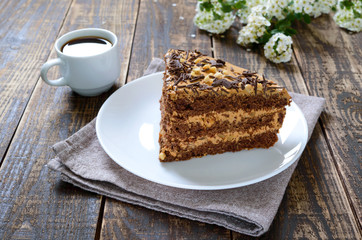 Chocolate cake with nut cream on a wooden table. A piece of cake on a plate and a cup of coffee.
