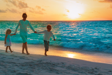 father with son and daughter walk on beach at sunset
