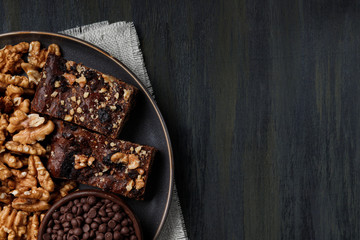 chocolate and walnut brownie next to walnuts and chocolate on a plate in the foreground, healthy food during quarantine at home