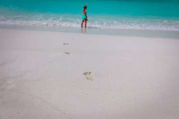 little girl walking on beach leaving footprint in sand