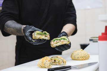 Deep fried sushi burgers in chef's hands. Takeaway food, fastfood kitchen: cook in the commercial kitchen holds a ready meal