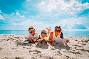 mother with son and daughter reading books at beach