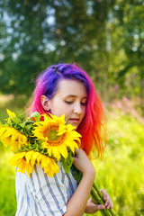 Naklejka premium Pink and lilac strands of hair. A beautiful happy teenage girl with a sunflower enjoys nature and laughs on a summer field. The sun's glare, the sun's rays, the sun's radiance. Illuminated