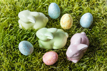 Easter composition with three porcelain bunnies with colored eggs on green grass moss.