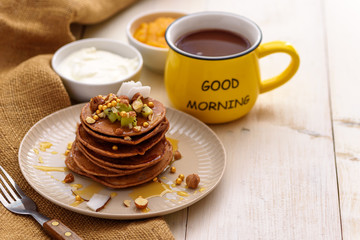 chocolate homemade pancakes with maple syrup, nuts, yellow Cup, sour cream and mango jam on table, delicious Breakfast concept, good morning, copy space