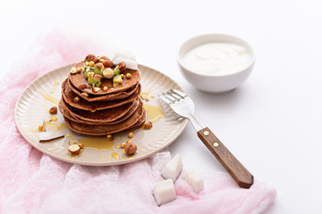 chocolate homemade pancakes with maple syrup, nuts, kiwi on plate on white background with pink gauze, beautiful Breakfast in morning