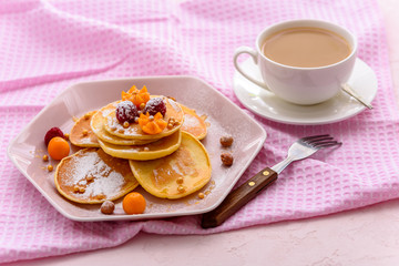 homemade pancakes with raspberries, physalis, powdered sugar on pink napkin with Cup of tea or coffee