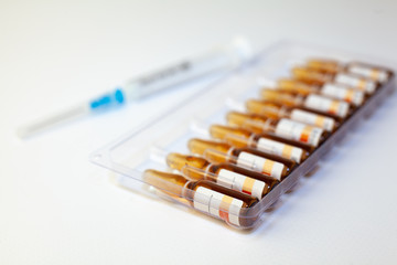 Medical drug ampules and syringe awaiting injection on white background, selective focus close up
