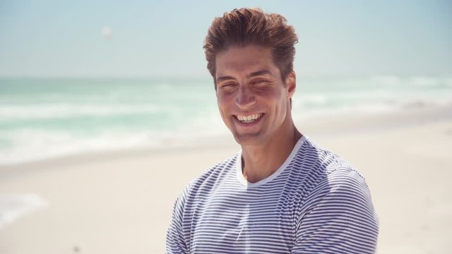 Portrait of handsome young man wearing sunglasses and looking at camera. Portrait of joyful man enjoying summer holiday at beach. Young casual man in shades with big grin and copy space.