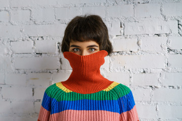 Portrait of a young woman in a multicolored sweater, covering her face with a sweater . The concept...