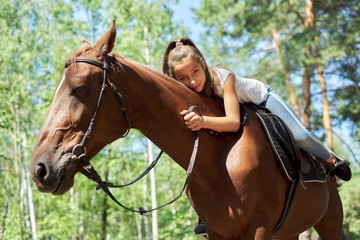 Girl child riding horse, summer horse ride in the forest, girl lovingly hugged horse