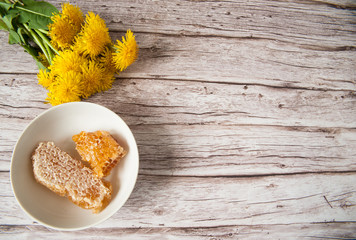 A bouquet of yellow dandelion flowers and a Cup with honey combs on a wooden background. Alternative medicine, medicinal herbs. Selective focus. Free space.