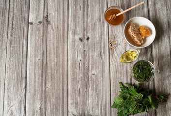 Natural home skin care. Preparing a face mask. Leaves and decoction of nettle dioecious, honey and olive oil close-up on a wooden background. Top view. Free space.