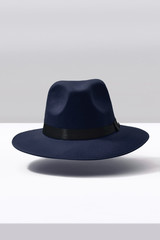 Subject shot of a blue fedora hat decorated with a black silk band with a bow. The stylish hat is hovering in the air under the white surface against the gray backdrop.