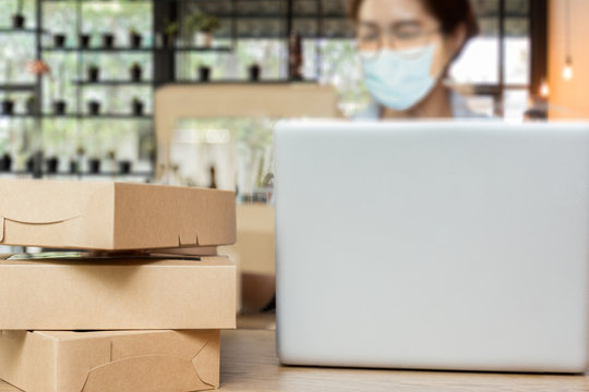 Selected focus parcel box on table with woman wearing medical mask work on laptop at home.