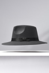 Subject shot of a gray fedora hat decorated with a black silk band with a bow. The stylish hat is hovering in the air under the white surface against the gray backdrop.