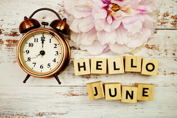 Hello June with alarm clock on wooden background