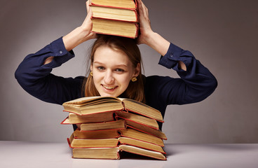 Woman sitting at the table and holding a book over her head on a dark background. The concept of learning.