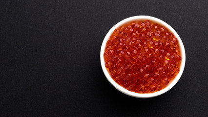 Red caviar on black stone background with copy space, top view