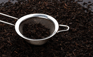 Metal tea strainer with dry black tea leaves
