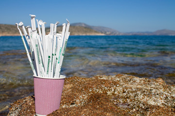 Fototapeta na wymiar Paper drinking straws in paper cup outside on rocks next to sea