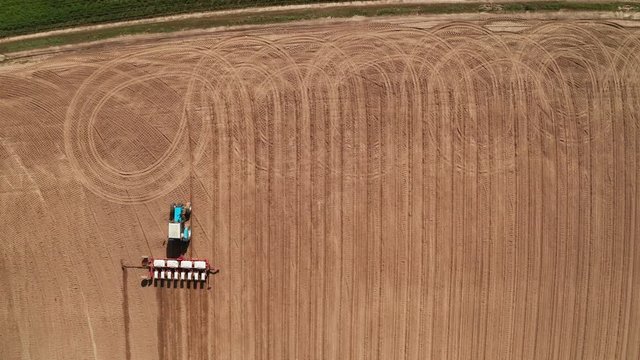 Aerial view of tractor with mounted seeder performing direct seeding of crops on plowed agricultural field. Farmer is using farming machinery for planting process, top view