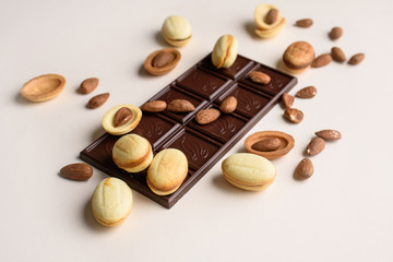 A bar of chocolate lies on a light background with almonds, walnuts, nuts with boiled condensed milk. View from above, place for text. Flat lay