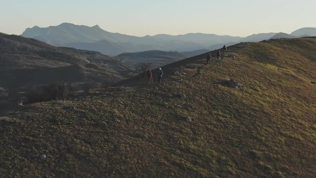 aerial shooting of a group of people walking along a trail on top of a hill at the sunset
