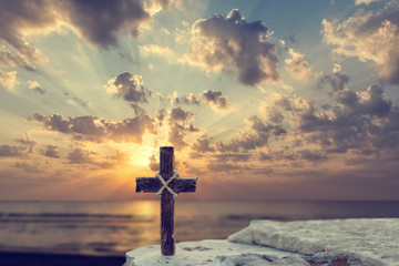 Wooden Christian cross on rocks against beautiful golden sunrise above the sea